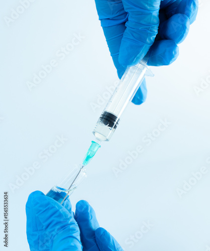 Gloved hands drawing liquid medication from an open glass ampoule using a syringe. Sterile medical procedure suitable for training, treatment, or pharmaceutical visuals.