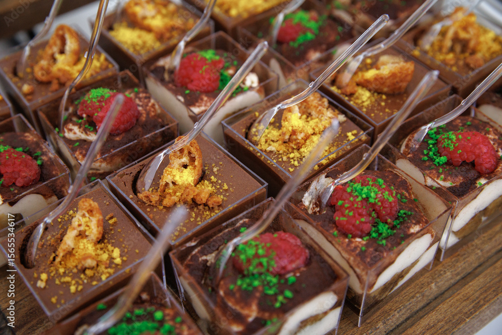 Tiramisu cups topped with fresh raspberries and colorful crumbs served on a wooden platter. Small spoons are ready for enjoyment, highlighting the dessert's inviting presentation. Tiramisu cups topped with fresh raspberries and colorful crumbs served on a wooden platter. Small spoons are ready for enjoyment, highlighting the dessert's inviting presentation.