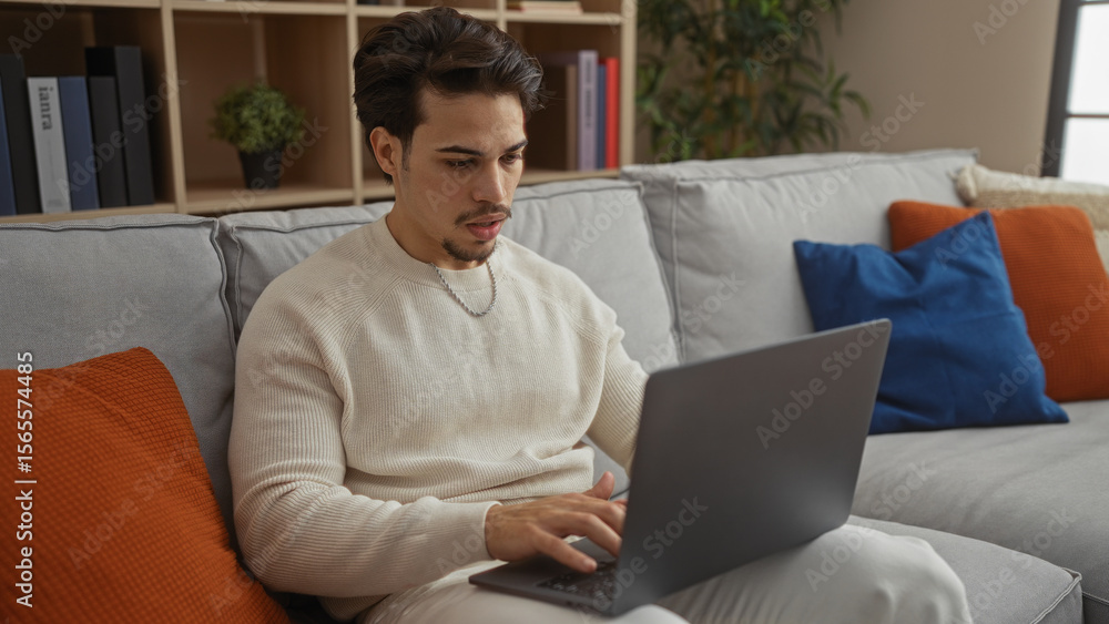 Young man using laptop in a cozy living room setting with stylish decor including colorful pillows and indoor plants, suggesting a relaxed and modern home environment. Young man using laptop in a cozy living room setting with stylish decor including colorful pillows and indoor plants, suggesting a relaxed and modern home environment.