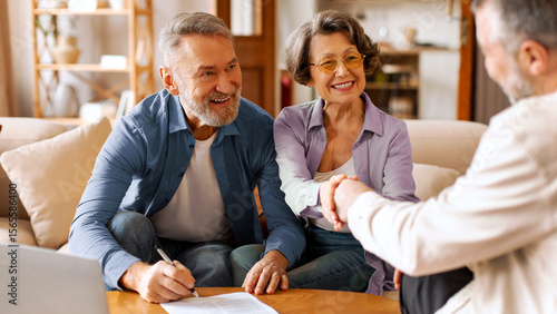 Happy senior couple making financial insurance estate deal, satisfied customers shaking hands with broker, meeting bank manager agree on investment contract