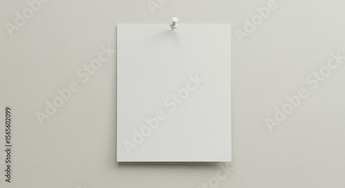 A rectangular, blank, white paper is pinned to a light beige wall with a small, white tack, creating a simple visual
