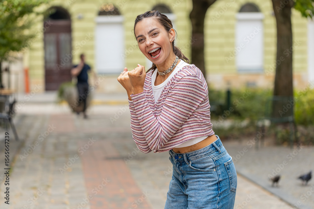 Fototapeta premium Excited happy woman tourist shouting, celebrating success, winning, goal achievement, good news, lottery jackpot luck, victory outdoors. Young girl walking on urban city street. Town lifestyles