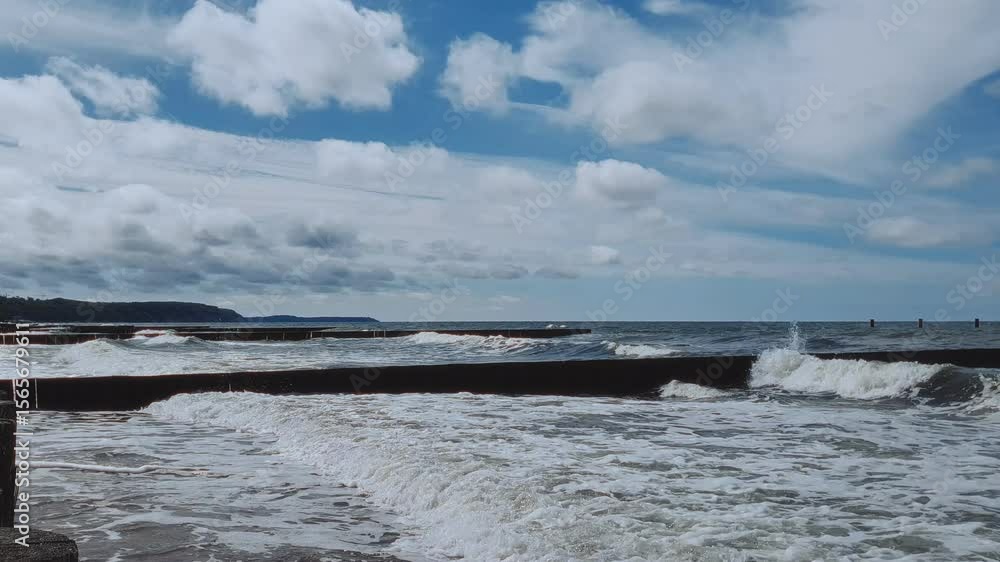Serene seaside landscape of Baltic sea coast with stormy waves rolling on empty beach and old wooden breakwater under dramatic cloudy sky at summer day. No people seascape natural background. Serene seaside landscape of Baltic sea coast with stormy waves rolling on empty beach and old wooden breakwater under dramatic cloudy sky at summer day. No people seascape natural background.