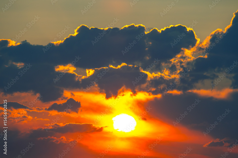 Fototapeta premium Dramatic sunset with a silhouetted cloud partially covering the sun. The warm gradient of orange and yellow tones creates a stunning contrast against the darker sky.