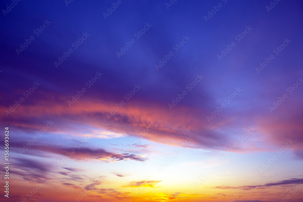Fototapeta premium Dramatic sunset sky featuring golden, fiery clouds against a deepening blue background. The rich colors and dynamic cloud formations create a stunning natural display.