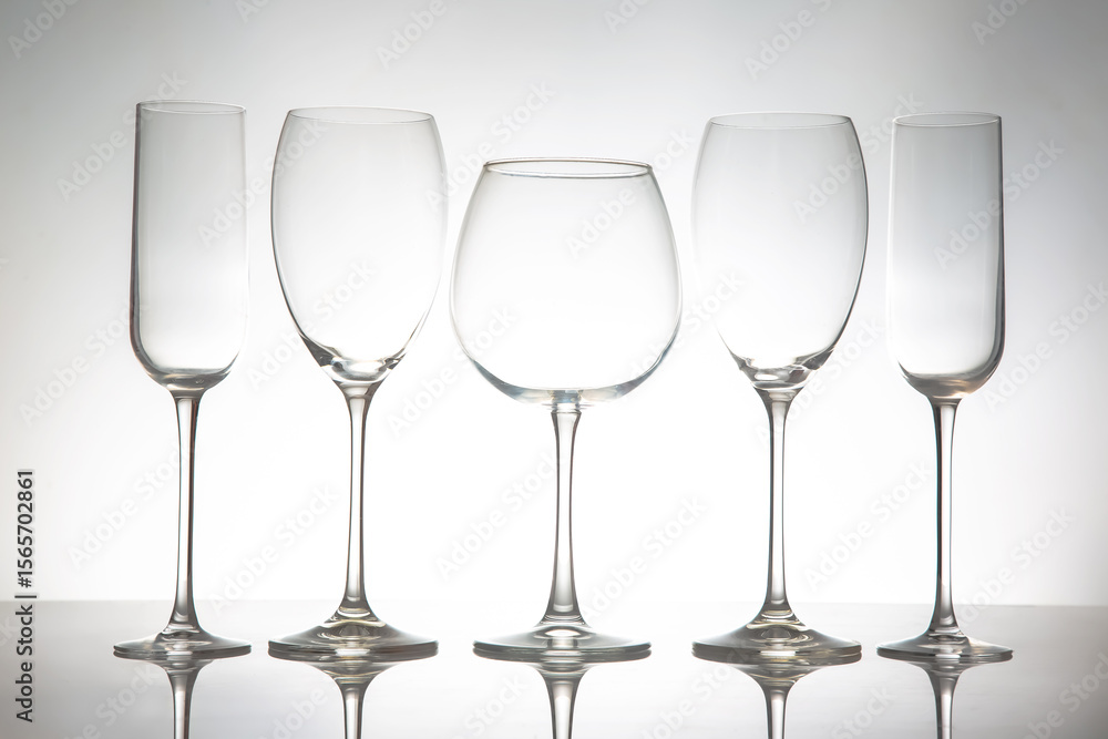 A sleek lineup of five elegant, empty wine glasses with long stems, reflecting on a glossy surface against a soft gray background, perfect for dining or event themes. A sleek lineup of five elegant, empty wine glasses with long stems, reflecting on a glossy surface against a soft gray background, perfect for dining or event themes.