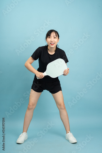Young girl in sports outfit poses with a paddle in a bright blue studio setting during a playful activity session