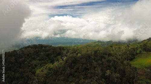 Sweeping over lush foothills, the lens captures dense canopy and scattered fields as giant white clouds roll overhead, briefly unveiling distant valleys around Mount Apo.