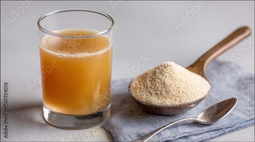 Benefits of Bone broth. Fresh beverage in a glass next to a spoonful of powder on a textured background.
