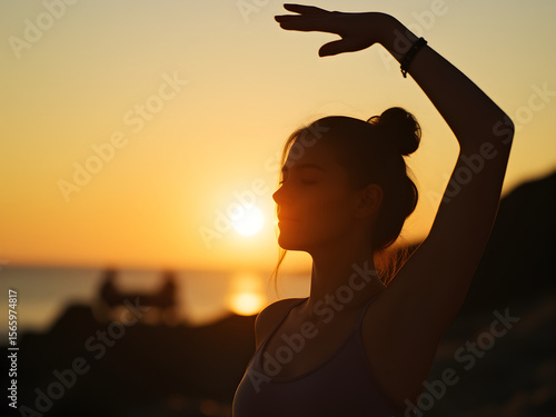 A woman is standing on a beach with her arms outstretched, looking at the sun