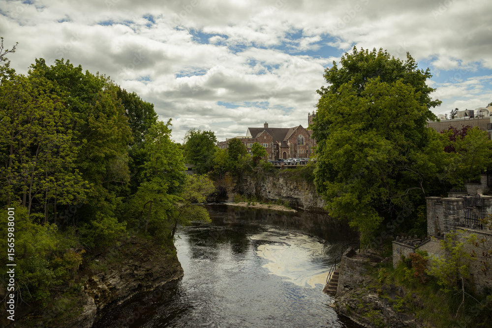 Fototapeta premium Fergus - town in Ontario on the Grand River, popular tourist town with beautiful old stone houses, a waterfall, and ancient bridges. A tourist magnet. Summer sunny day with cloudy sky. Ontario, Canada