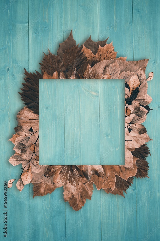 Fototapeta premium Flat square turquoise frame is resting on painted wood surface surrounded by brown leaves