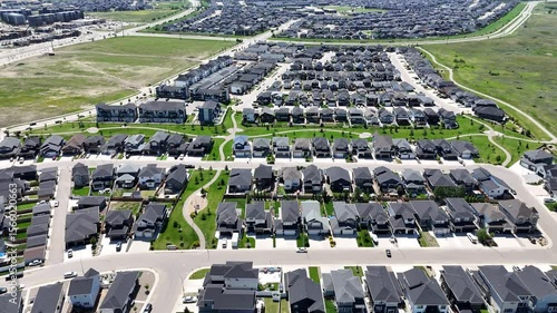 Residential neighborhood with many houses and a few cars. The houses are mostly white and the street is lined with trees