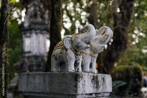 Twin white elephant statues with gold and red details on a stone pedestal – traditional Thai decorative figures in a forest setting.
