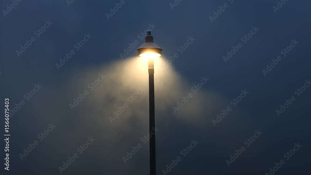 Street Lamp Illuminating Through Thick Fog at Night Creating a Moody Atmosphere Against a Dark Blue Gray Sky Street Lamp Illuminating Through Thick Fog at Night Creating a Moody Atmosphere Against a Dark Blue Gray Sky