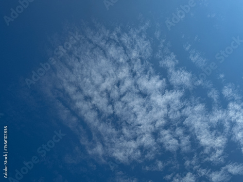 Fotografie Clear blue sky adorned with scattered, wispy white altocumulus clouds, creating a peaceful and expansive natural backdrop