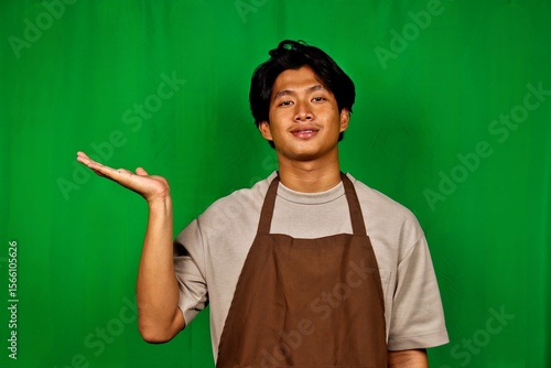 Young Man Wearing Apron Standing in Front of Green Screen with Confused Expression