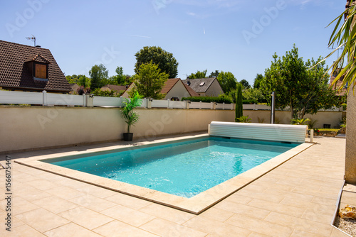 Quadro su tela Piscine privée avec margelles en pierre beige, entourée de verdure et équipée d’un rouleau pour bâche, dans un jardin paysager