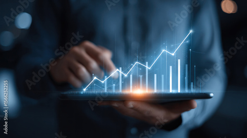 Modern business analyst holding tablet displaying rising charts and glowing economic indicators, digital interface elements float above screen, corporate background