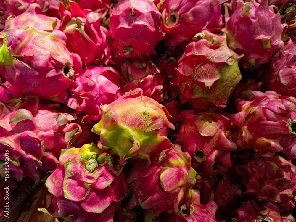 Fototapeta premium Close-up view of fresh dragon fruits with vibrant pink skin and green-tipped scales, stacked together in a market or grocery store setting