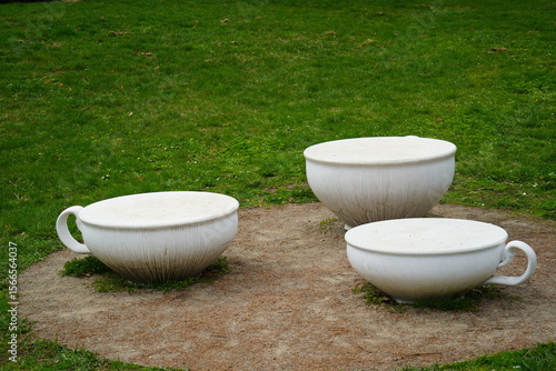 Creative seating arrangement showcases oversized white teacups in a vibrant green garden during a sunny afternoon, inviting relaxation and playful imagination