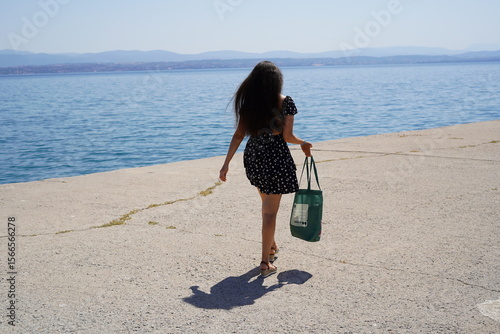 Joyful stroll by the tranquil water on a sunny day with a vibrant outfit and a stylish bag in hand, capturing carefree moments of summer bliss