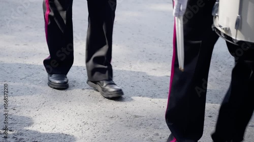 A lively group of uniformed percussionists marches in synchronization on a paved street, capturing the rhythmic energy and movement of a vibrant public performance.