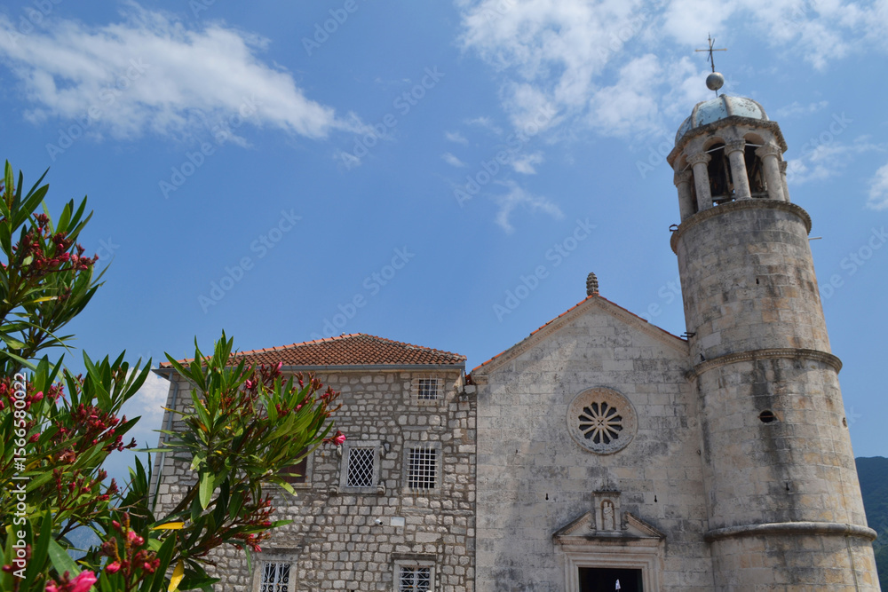 Fototapeta premium Close-up of Historic Stone Bell Tower and Church Facade in Perast, Montenegro, under Blue Sky