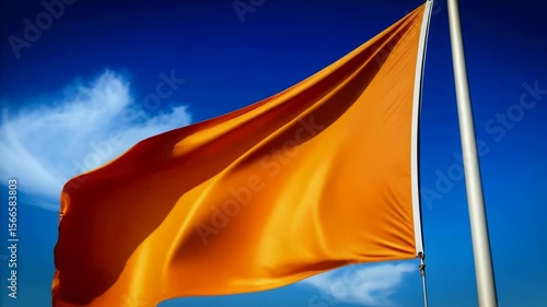 Bright orange warning flag waving against vivid blue sky, potential hazard advisory and caution, coastal safety banner on pole, clear day outdoors