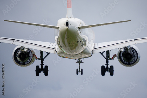Rear view of commercial jet airplane on final approach with landing gear deployed, aviation photo of twin-engine aircraft in flight with flaps extended and turbines visible