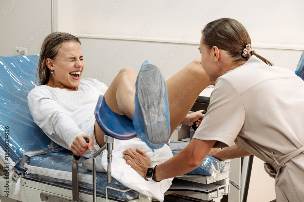 Fototapeta premium In a delivery room, a young woman is pushing during labor, face tense. Concept of birth effort and the strength of the female body.
