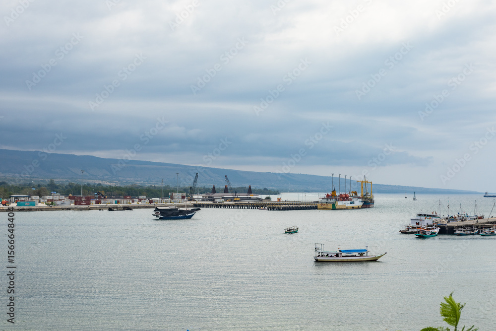 Fototapeta premium Sumba, Indonesia – 07. 04. 2025 – It's still daytime, but the weather is cloudy. Two seaports in Waingapu are visible in a single view, with small and large ships moored around them