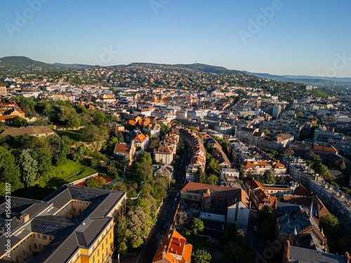 Photography Drone photo from Castle District facing inland over Buda neighborhoods, showing Csalogány Street area, District 1 rooftops, Széll Kálmán tér, and distant hills of Districts 2 and 3