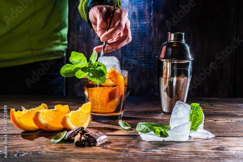 Mixing a cocktail with a bartender's spoon. Bartender mixes a cocktail. Large pieces of ice and mint in a glass. Spoon in hand.