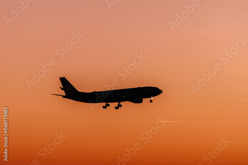 Silhouette of a passenger airplane landing at sunset, flying through a vivid orange sky. Peaceful scene representing air travel, freedom, and evening light.