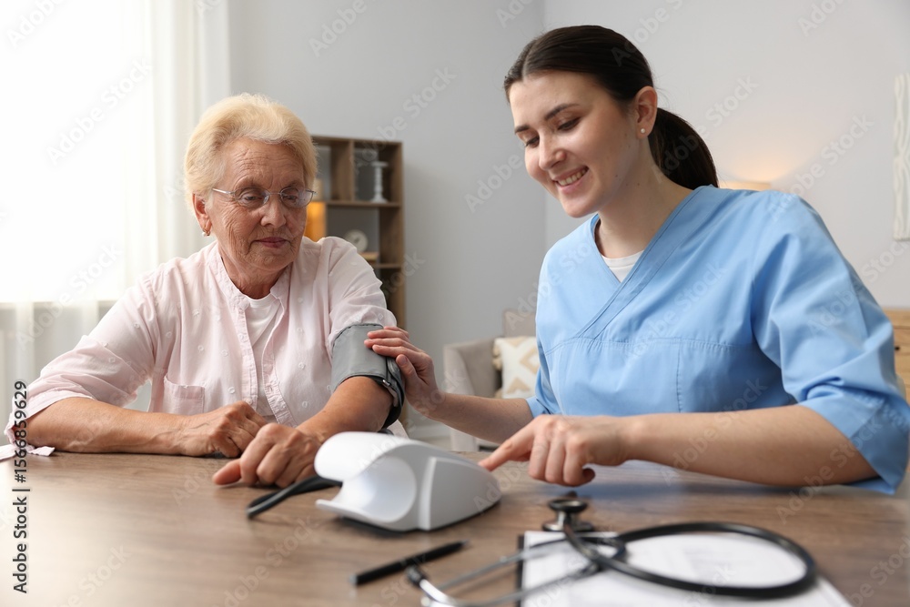 Obraz premium Nurse measuring patient's blood pressure at wooden table indoors. Home health care service