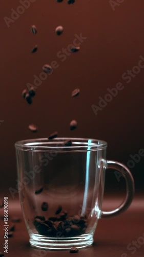 Grains de café remplissant un mug transparent et débordant, au ralenti sur fond marron