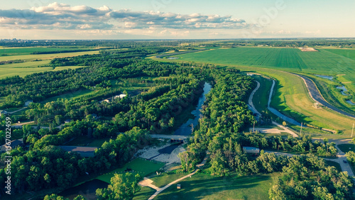 Epic aerial photo of a vast river valley with lush forests, green farmland, and a city skyline on the distant horizon at sunset.