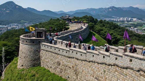 Tourists Explore Historic Fortress Wall with Flags and Mountain Backdrop in Korea
