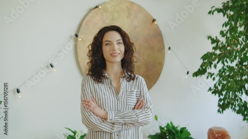 Smiling woman standing confidently in a bright room adorned with plants and warm lights, showcasing a relaxed yet professional atmosphere