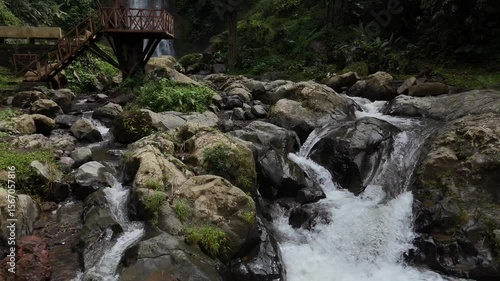 Scenic drone view of Gitgit waterfall and a stream flowing over rocks in a lush, natural setting