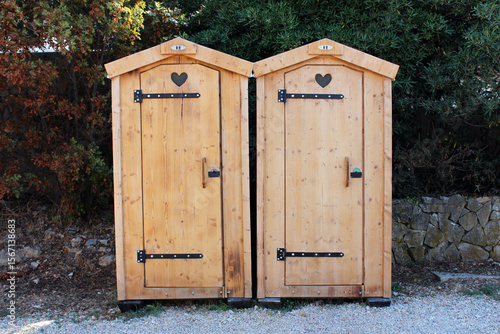 Tableau sur toile Two side-by-side wooden outhouses with heart-shaped ventilation cutouts stand on
