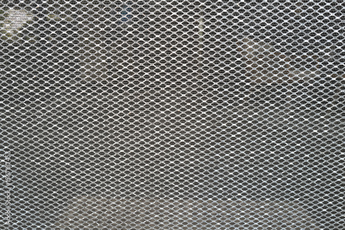 Close-up of a metallic mesh screen forming a repetitive diamond-shaped pattern. The background is softly blurred, emphasizing the texture and geometry of the netting. Ideal for illustrating concepts o