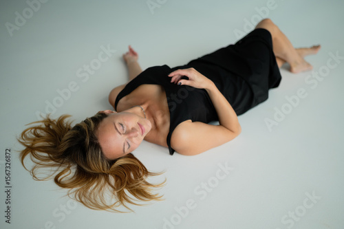 A beautiful girl in a black dress is lying on a white floor	
