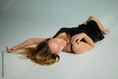 A beautiful girl in a black dress is lying on a white floor