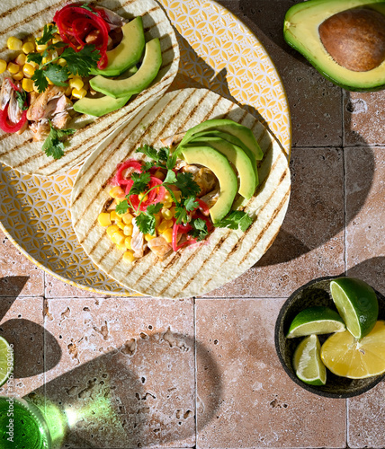 Top view of two tortillas with avocado, meat, and fresh herbs on bright background. Mexican street food, fresh and colorful meal.