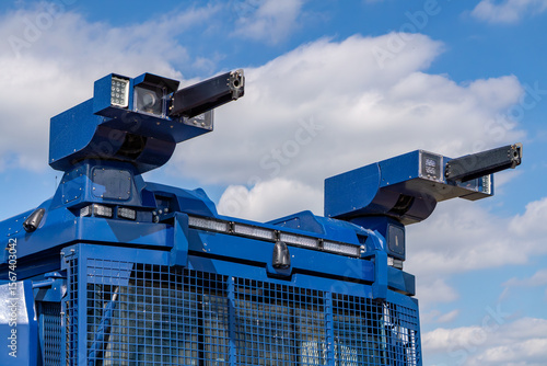 Riot control vehicle turret with water cannons and spotlights mounted on armored police truck against blue sky