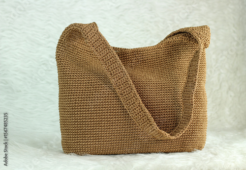 Crocheted handmade milky brown bag on furry white blanket.