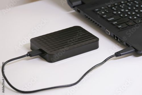 Fotografie Close-up of an external hard drive connected to a laptop on a white table