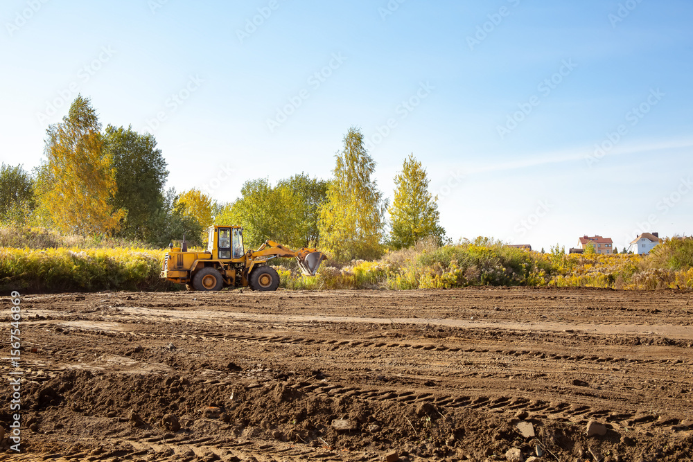 Fototapeta premium Yellow bulldozer at a construction site. Big wheel excavator leveling and clearing the land plot side view. Moving earthworks soil. Copy space. Building area. Special transport. High quality photo.